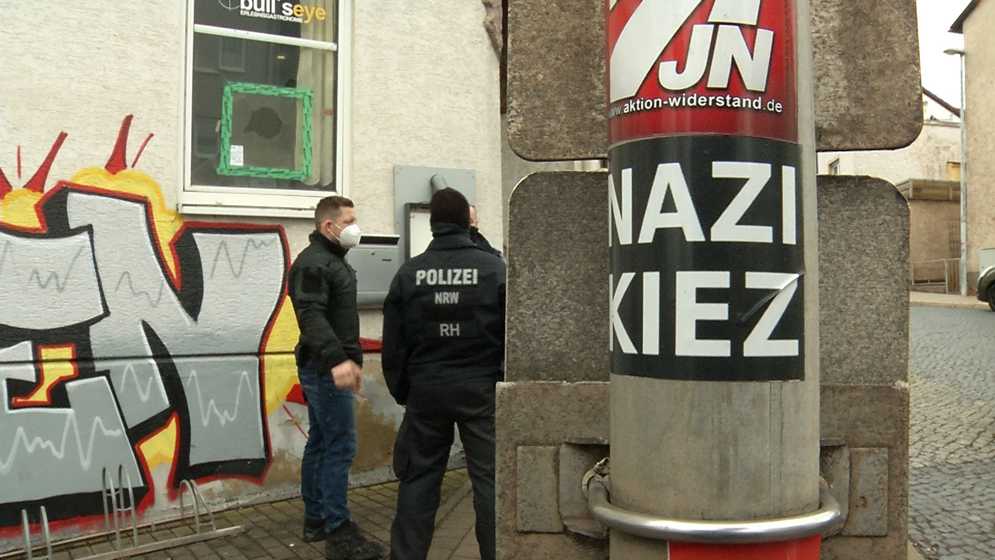 Polizisten Stehen Vor Der Gaststätte «Bull's Eye». An Einem Pfahl Ist Ein Aufkleber Mit Der Aufschrift «Nazi Kiez» Zu Sehen.