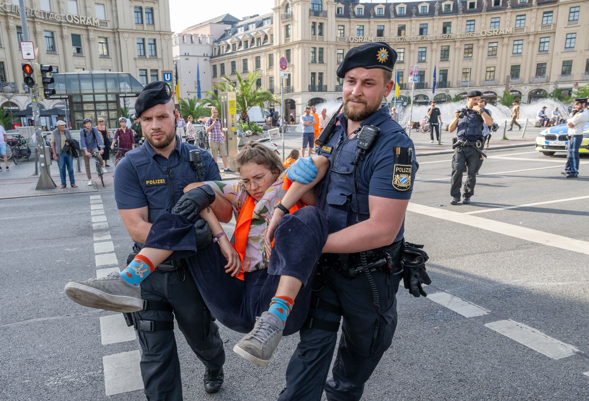 Polizisten Tragen Auf Der Kreuzung Am Stachus In Der Münchener Innenstadt Aktivisten Der Letzten Generation Weg. Ihre Aktionen Werden Teilweise Verboten.