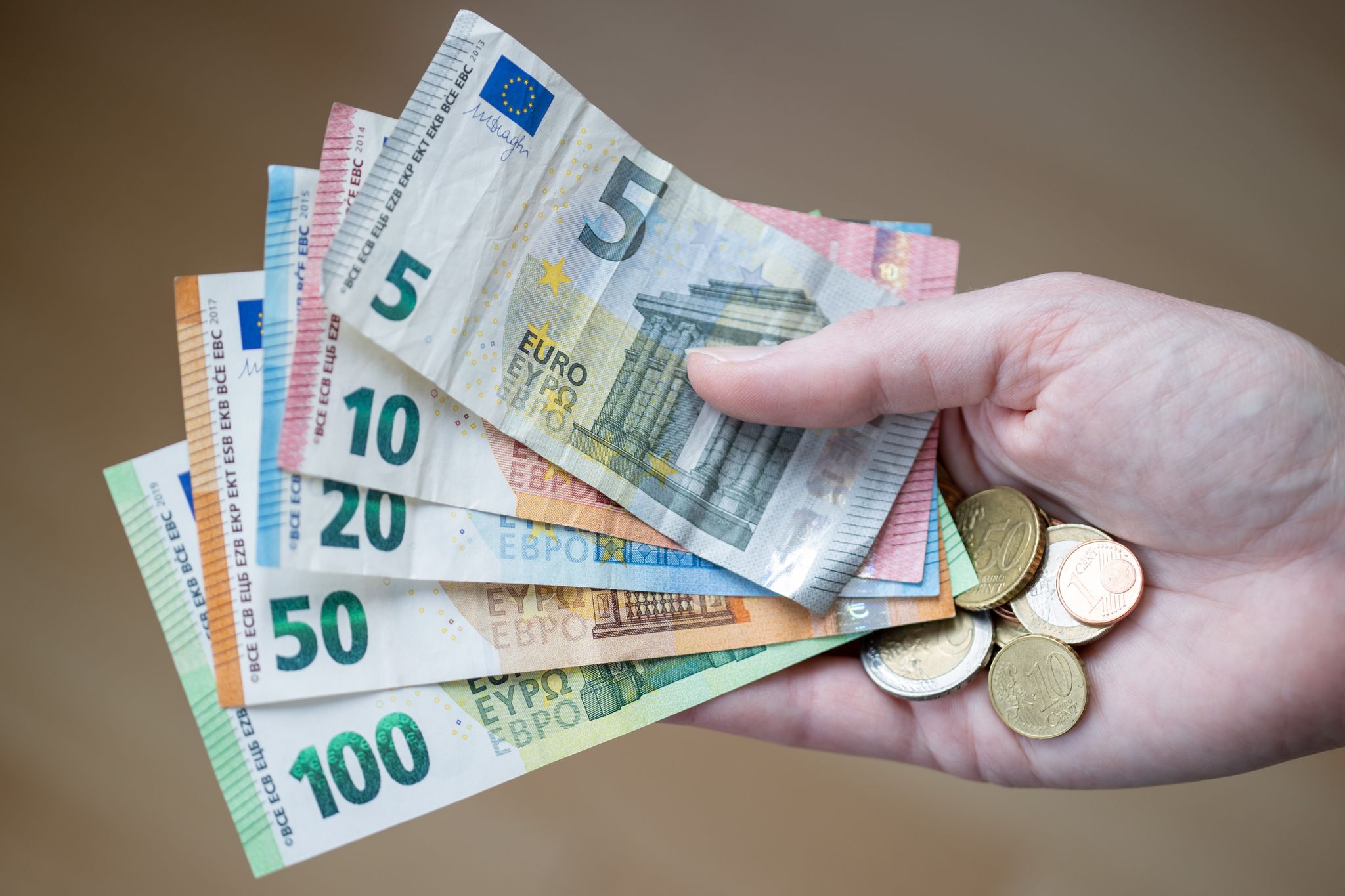 Eine Frau Hält Geldscheine Und Münzen In Der Hand.