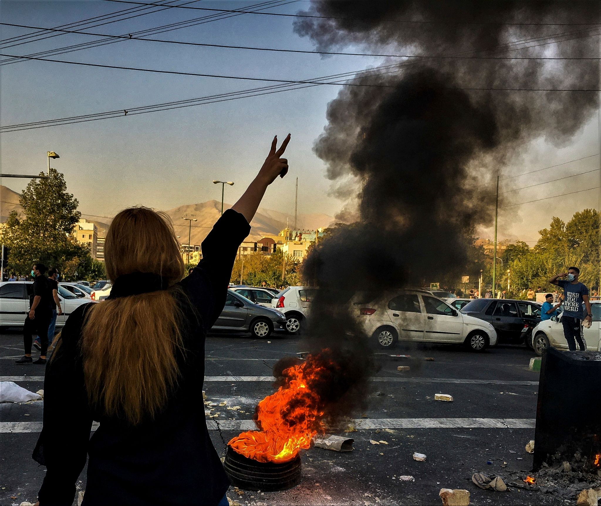 Eine Frau Steht Während Einer Demonstration In Teheran Vor Einem Brennenden Autoreifen Und Zeigt Das Victory-Zeichen.