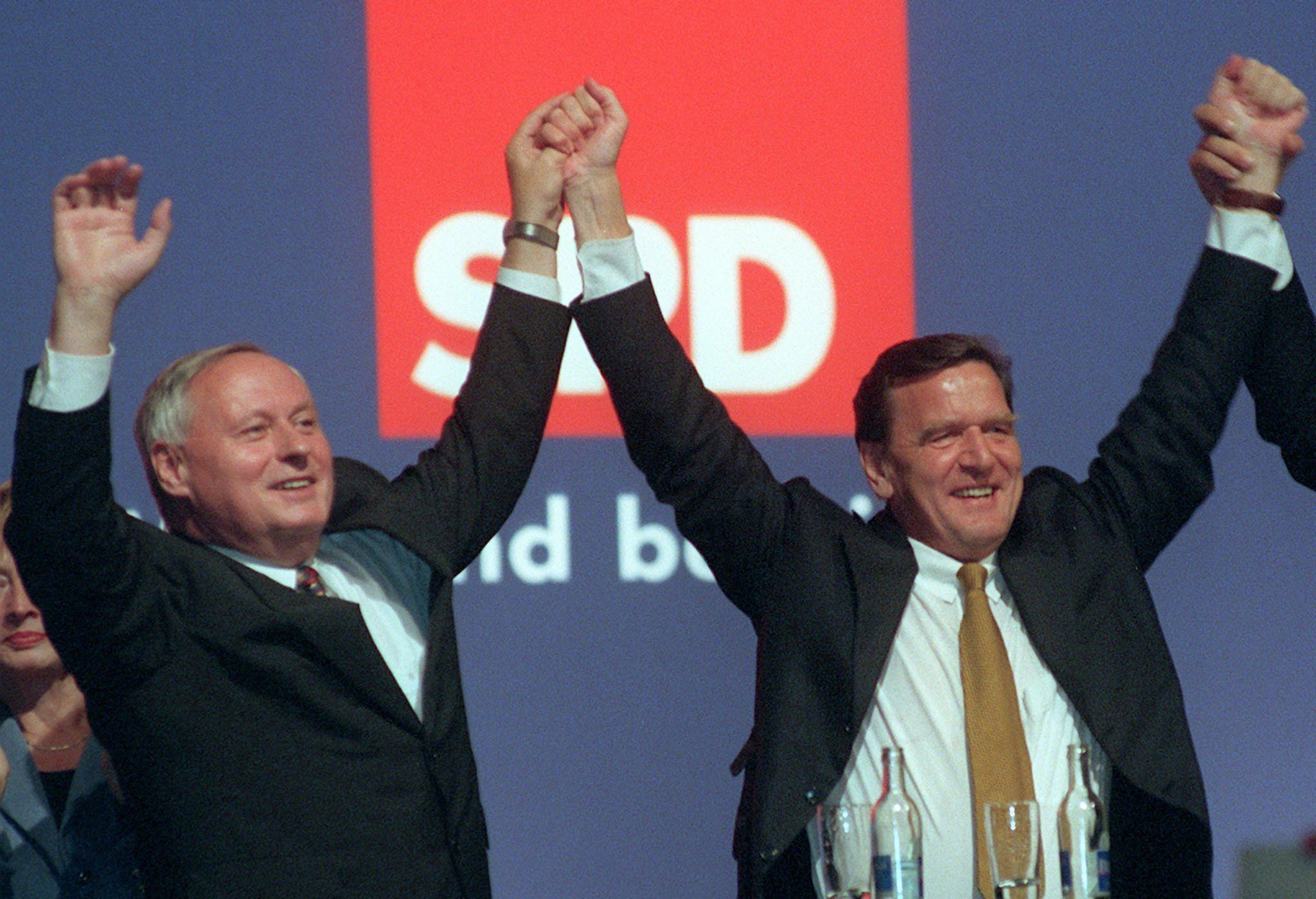 Gerhard Schröder (r) Und Oskar Lafontaine Halten Sich Bei Einer Veranstaltung An Den Händen.