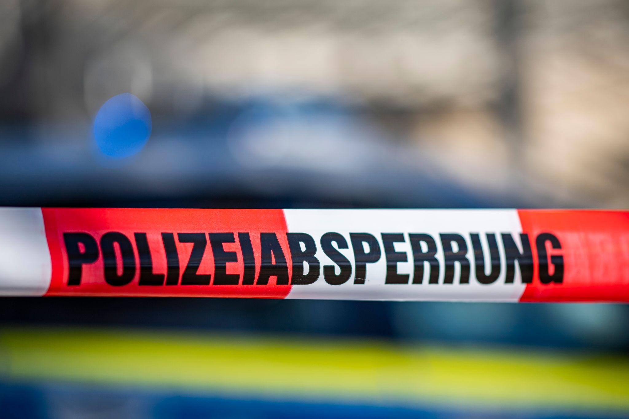 Ein Absperrband Mit Der Aufschrift «Polizeiabsperrung» Ist Vor Einem Polizeiwagen Aufgespannt.