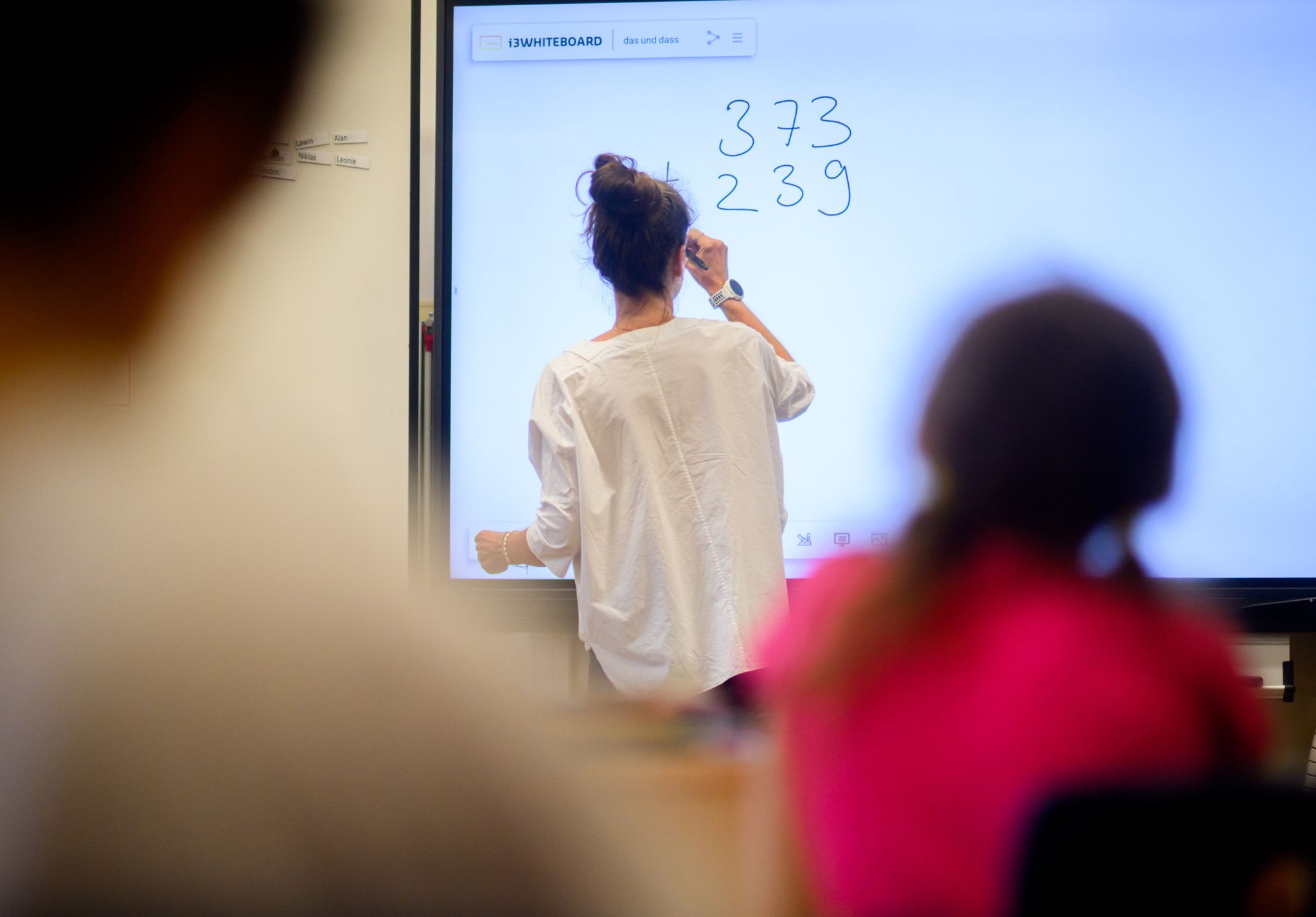 Eine Lehrerin Schreibt Eine Mathematikaufgabe Auf Eine Digitale Schultafel Im Klassenraum Einer 4. Klasse Einer Grundschule.