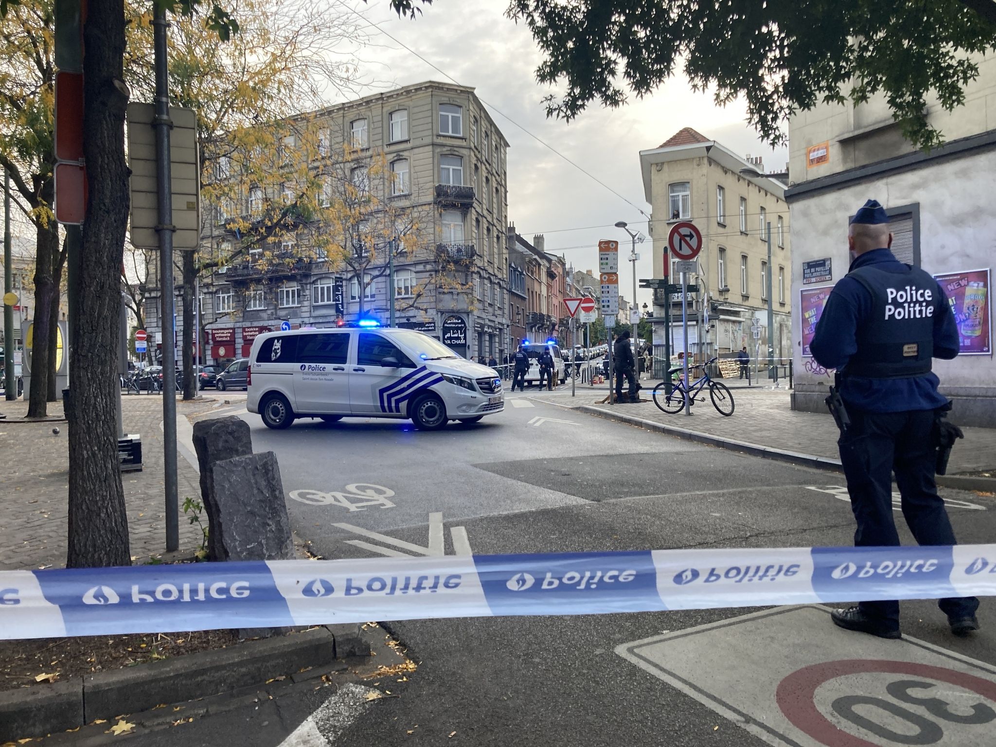 Die Polizei Sperrt Eine Straße, Während Ein Polizist Hinter Absperrband Wache Steht.