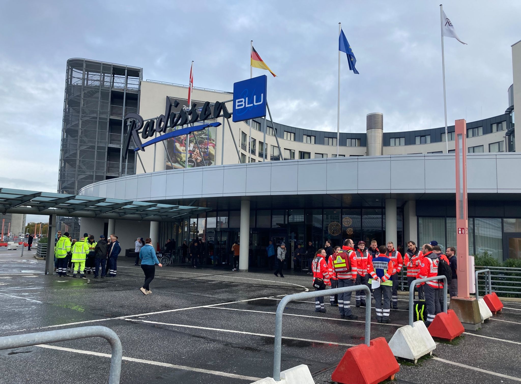 DRK-Einsatzkräfte Stehen Vor Dem Hotel Radisson Blu, In Dem Passagiere Untergebracht Wurden.