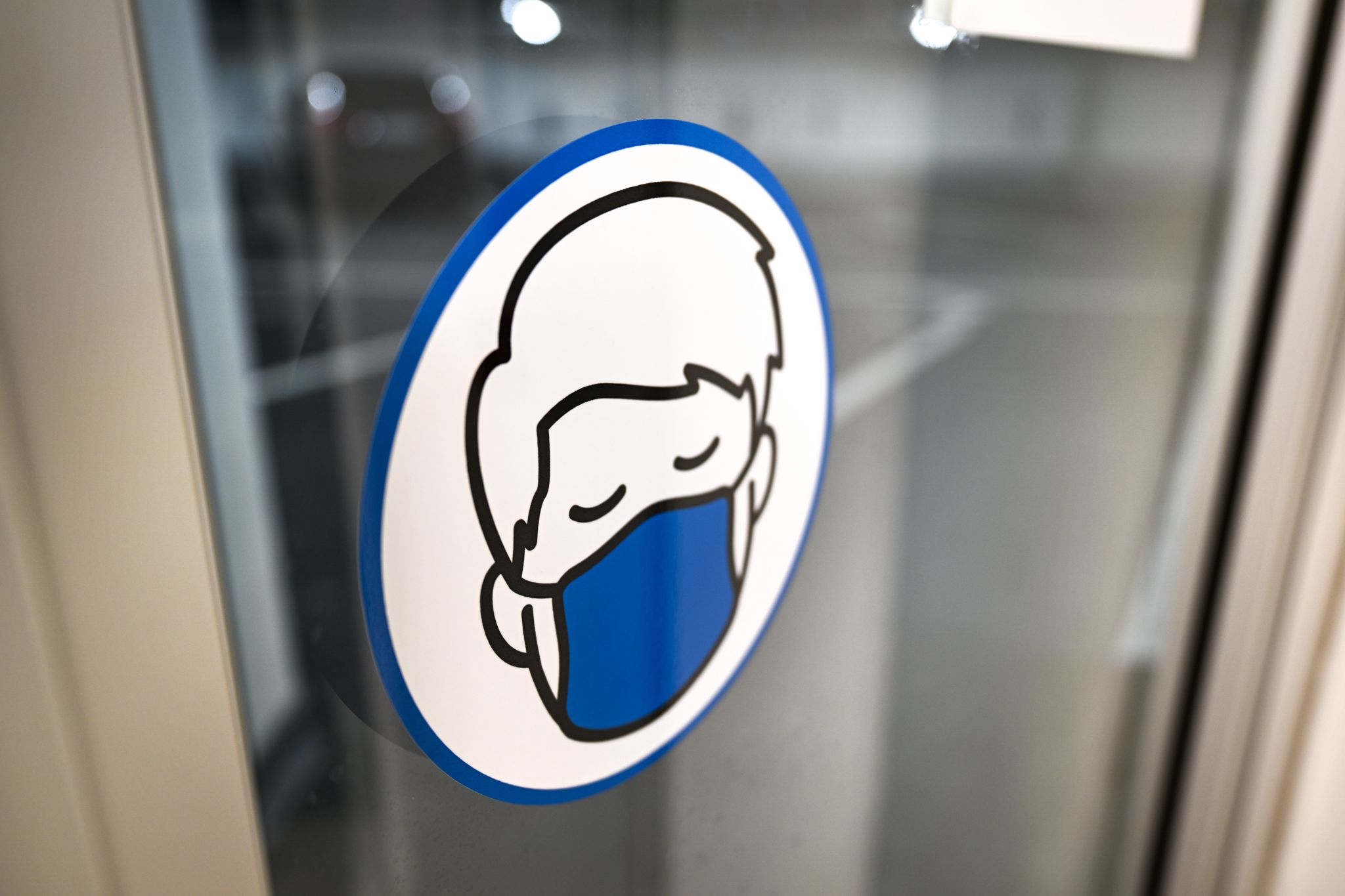 Ein Aufkleber An Einer Glastür Weist Auf Das Tragen Einer Maske Hin.